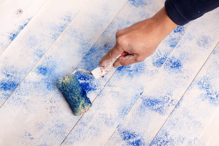 s hand with paint roller is painted blue color on white wooden b