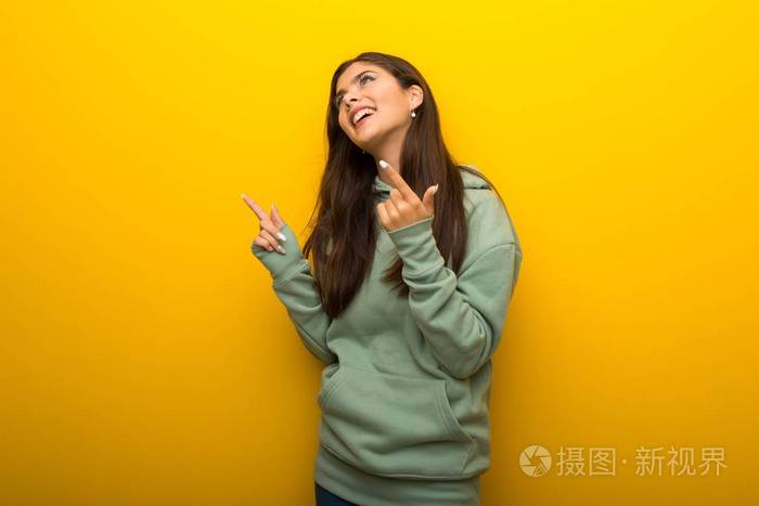 黄色背景绿色运动衫的少年女孩用食指指着,抬头看