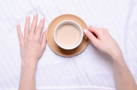 妇女拿着一杯咖啡在白色亚麻布床
