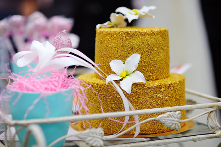 用白糖花装饰的金色婚礼蛋糕。 婚礼派对甜蜜的桌子