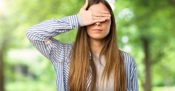 带条纹衬衫的年轻女孩用手遮住眼睛。 不想在户外看到什么