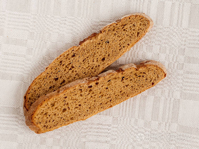 切片黑麦面包，在灰色亚麻桌布上有一个令人开胃的脆棕色外壳。 美味有用和营养。 直接上方的视图关闭。