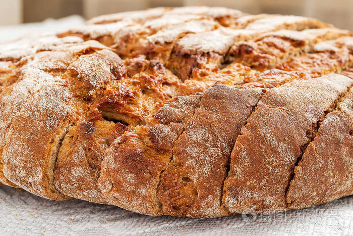 切片圆形黑麦面包，在灰色亚麻桌布上有一个开胃的脆皮棕色面包皮。 美味有用和营养。 正面视图关闭选择性焦点。