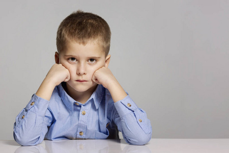 手撑起的头悲伤的男孩坐在他的头上,双手紧闭着灰色的背景照片