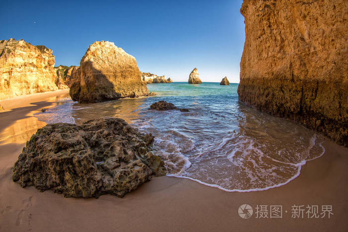 著名的海滩岩层位于葡萄牙阿尔加维的海洋中。 前景中美丽的石头和波浪。