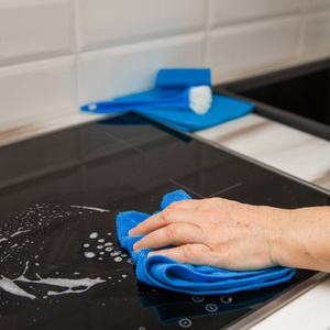 s hand with a blue microfiber cloth rubs a glass ceramic plate i