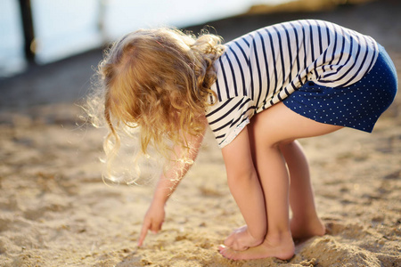 夏天，小女孩在湖边散步时玩沙子。宝宝在沙子上画手指。积极的家庭时间自然。