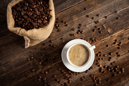 咖啡杯与咖啡种子在老式的木桌和下垂的豆子形成顶部。
