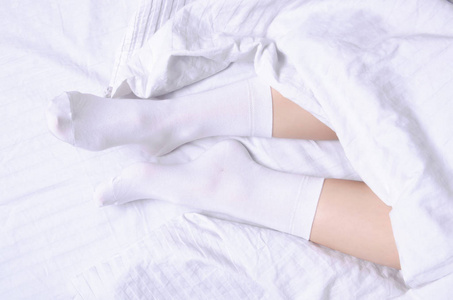 女性腿在白色袜子在白色亚麻布床