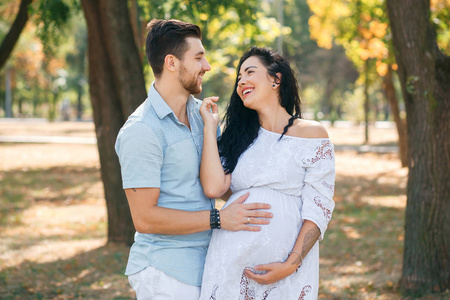 怀孕的女孩和她的丈夫在公园里拥抱和亲吻，享受美丽的天气。