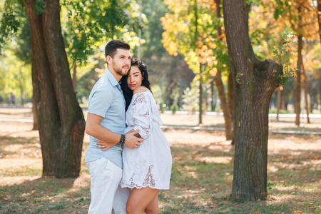 怀孕的女孩和她的丈夫在公园里拥抱和亲吻，享受美丽的天气。