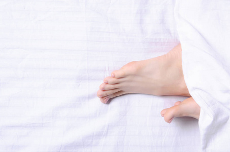 女性腿秀丽在白色床各种各样的女孩穿着浴袍躺在床上抬起腿女性的脚在