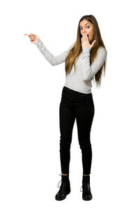 侧面惊讶年轻女孩手指指向侧面的完整镜头,孤立的白色背景上有一张