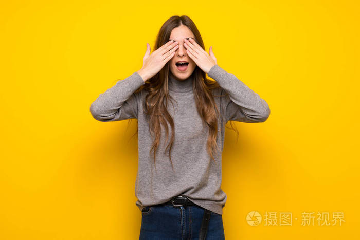 年轻的女人在黄色的墙上用手遮住眼睛惊讶地看到前方的情况