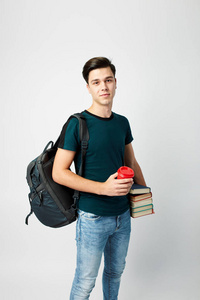 黑头发的家伙, 肩上背着黑色背包, 身穿黑色 t恤和牛仔裤, 手里拿着书, 手里拿着一个白色背景的红色塑料杯