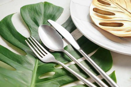 有盘子的银色餐具，桌子上有绿色的热带叶子