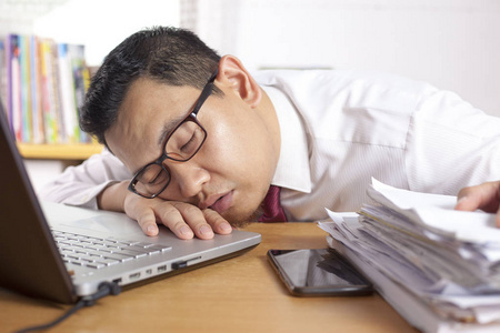 办公室疲劳这位亚洲商人因工作过度而疲劳,在办公室的笔记本电脑和