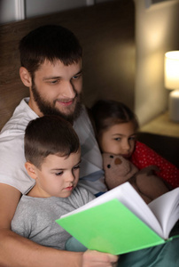 年轻的父亲为他的孩子们在床上看书