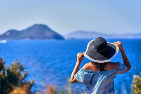 美丽的女人戴着沙滩帽，在阳光明媚的日子里，在火鸡胸前欣赏蓝天海景。 户外度假海景暑期旅游概念