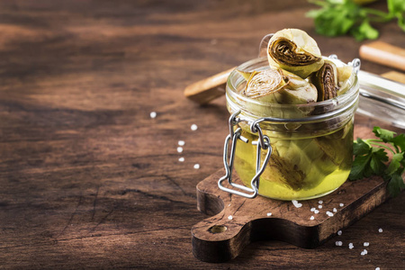 罐装洋蓟在橄榄油玻璃罐，乡村木制厨房餐桌背景，仍然生活，Dof选择焦点