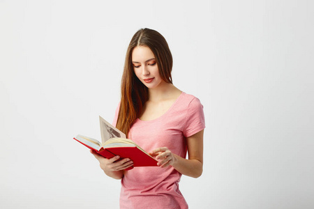 美丽的长头发的女孩穿着粉红色的 t恤阅读一本书在一个白色的背景在演播室