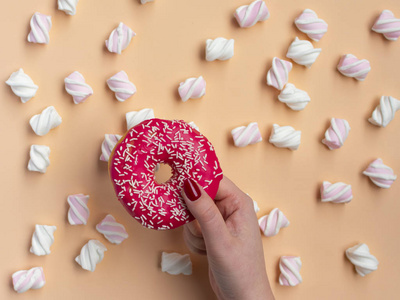 s hand holding donut with marshmallow on peach background