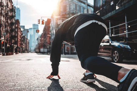 城市跑步者在城市街道上开始姿势的背面视图.