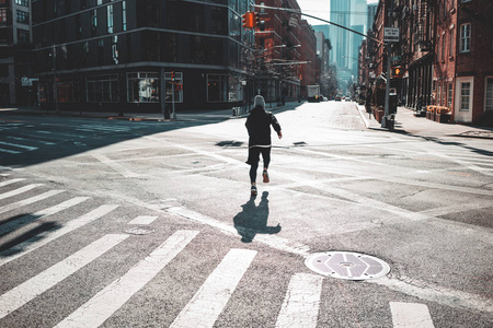 年轻的运动员穿过纽约的街道。 运动的人在阳光明媚的一天清晨快速奔跑穿过城市