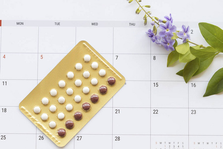 避孕丸避孕药女人为不想要宝宝而计划日历用紫花装饰平躺式背景白色