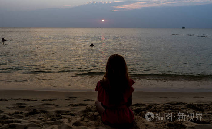 旅行女孩,留着长长的红头发,坐在海滩上,美丽的日