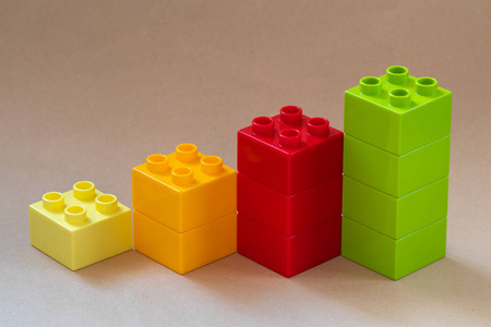 从米色背景上的彩色玩具块中生长条形图。 特写镜头。
