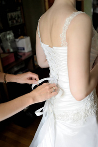 s hands tie a ribbon on the corset of a wedding dress.