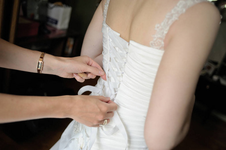 s hands tie a ribbon on the corset of a wedding dress.