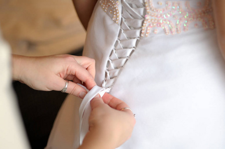 s hands tie a ribbon on the corset of a wedding dress.