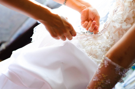 s hands tie a ribbon on the corset of a wedding dress.