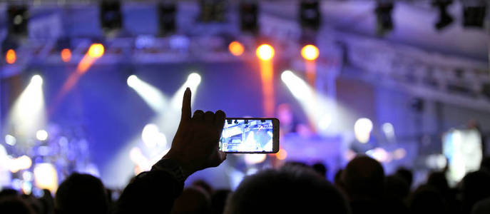 在用现代智能手机拍摄摇滚音乐会时，人们举起小手指的手