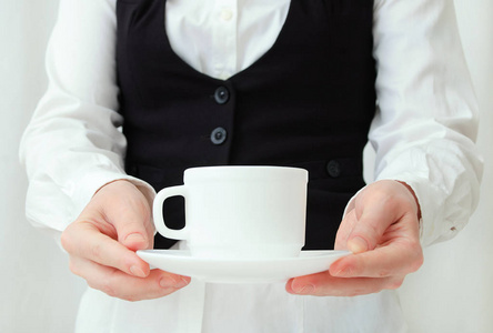 白种人女孩侍者穿着白色衬衫和黑色背心，手里拿着一对茶。