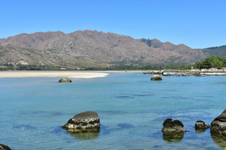 有山和树的海滩。 清澈的水，绿松石色的岩石和白色的沙子。 晴天蓝天。 加利西亚科鲁纳省西班牙。