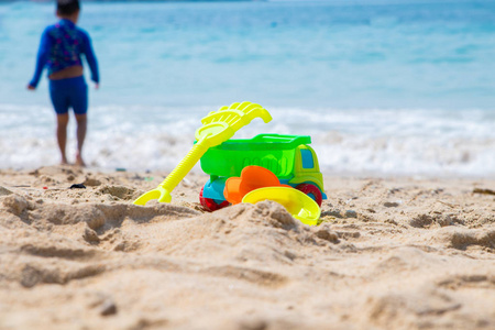 在阳光明媚的日子里, 儿童海滩玩具水桶铁锹机器汽车和铲子在沙滩上。男孩的剪影