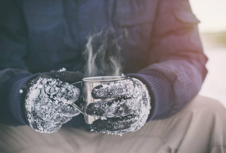 带热茶或咖啡的手套中男性手的侧面视图。 茶歇。 冬季时间概念