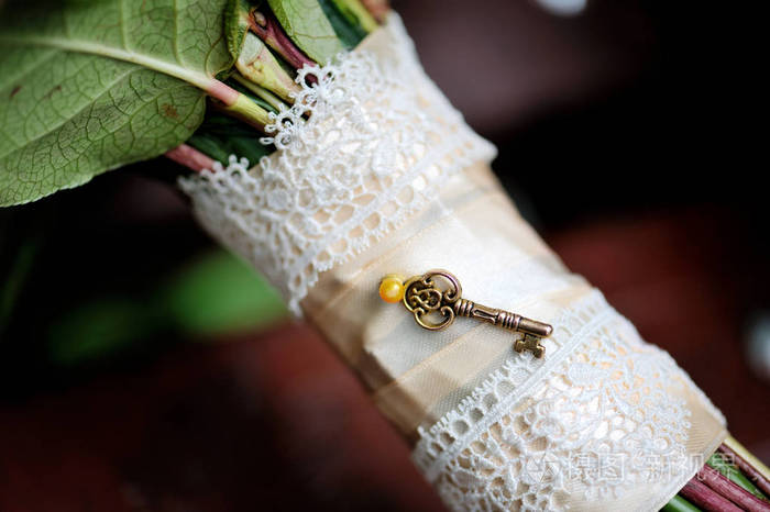 婚礼花束的花束腿,装饰着一条白色丝带和一把小的老式钥匙.