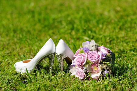 一束新娘和白色高跟鞋在草地上。 美丽多彩的婚礼花束。