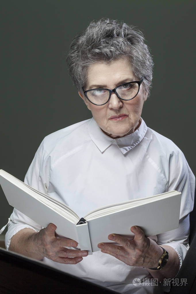 漂亮的灰发老年妇女带着可爱的微笑在家里轻松地看书