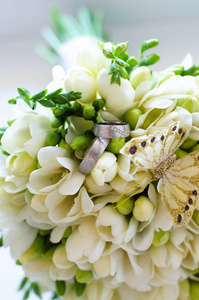一束白色的婚礼花束，有一只装饰性的蝴蝶和银色的结婚戒指。