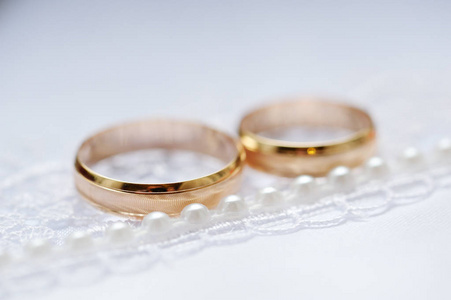 金色结婚戒指在白色织物上，有花边和珠子。 快关门。