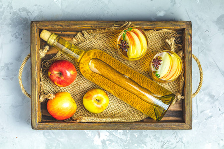 瓶装和玻璃杯自制有机苹果酒，新鲜苹果在盒顶视图轻同志混凝土台面。