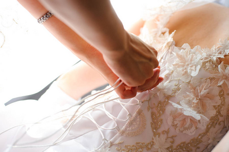 s hands tie a ribbon on the corset of a wedding dress.