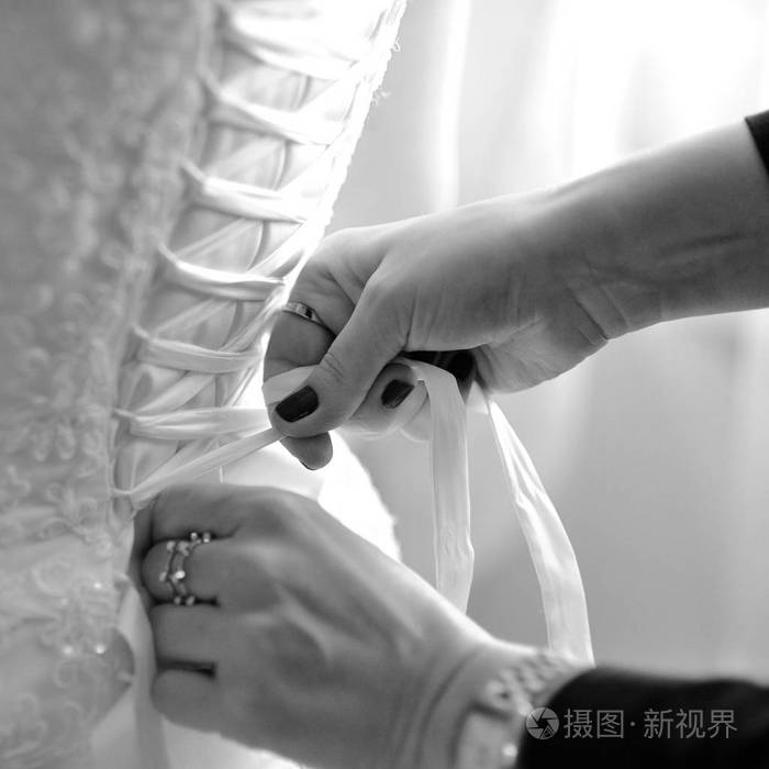 s hands tie a ribbon on the corset of a wedding dress. Black and