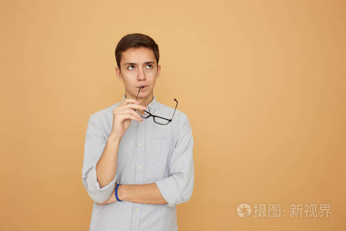 在演播室里, 穿着浅蓝色衬衫的体贴的家伙手里拿着眼镜站在米色的背景