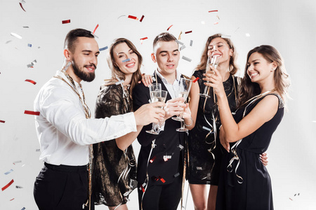 穿着时尚优雅服装的女孩和在一起, 在白色背景的糖果上用香槟酒拍打眼镜。派对时间